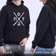 Худі пох*й чорного кольору, з капюшоном, на моделях чоловіка та жінки. Принт на грудях добре видно, обидва моделі стоять в профіль, показуючи манжети та кишеню-«кенгуру».