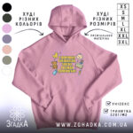 Худі помічник вихователя подарунок, ніжно-рожевого кольору, з капюшоном, з кишенею-«кенгуру», на фоні видно кольори інших худі. Принт на грудях яскравий, з малюнками і текстом.