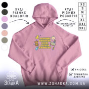 Худі помічник вихователя подарунок, ніжно-рожевого кольору, з капюшоном, з кишенею-«кенгуру», на фоні видно кольори інших худі. Принт на грудях яскравий, з малюнками і текстом.