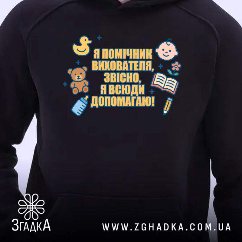 Худі помічник вихователя подарунок, чорного кольору, з капюшоном, на передньому плані видно принт з малюнками і текстом. Фон світлий, що підкреслює контрастність худі.