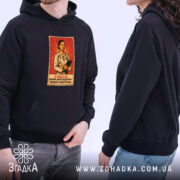 Худі стильний подарунок педіатру, темно-синього кольору, на фоні дві людини в худі, з капюшонами, принт з лікарем на червоному фоні добре видно, є кишеня-«кенгуру», манжети та пояс класичного стилю, ракурс з боку.