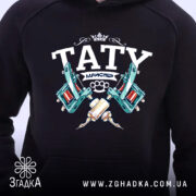 Худі тату майстер, чорного кольору, з капюшоном, з фронтального ракурсу, на фоні світлого кольору, з детальним принтом, що містить зображення тату машинок та напис 'TATY МАЙСТЕР', без кишені-«кенгуру», манжети виконані з еластичної тканини.