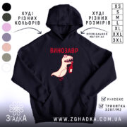 Худі з принтом динозавр, темно-синього кольору, зображене з ракурсу спереду, на фоні світлого простору. Принт з веселим динозавром, що тримає пляшку, виконаний у червоному та світло-кремовому кольорах. Кишеня-«кенгуру» розташована внизу, капюшон має класичну форму, манжети та пояс виконані в рибаній текстурі.