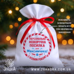 Мішечок іменний новорічний з червоною стрічкою на фоні ялинкових вогників.