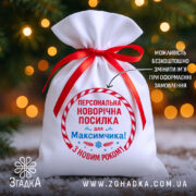 Мішечок іменний новорічний з червоною стрічкою на фоні ялинкових вогників.