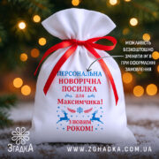 Мішечок іменний новорічний з червоною стрічкою на фоні ялинкових вогників.