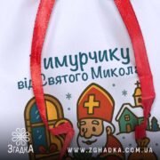 Мішечок подарунковий до Миколая — крупний план іменного друку та текстури габардину з червоною зав’язкою.