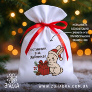 Мішечок подарунок від зайчика з червоною стрічкою на фоні ялинкових вогників