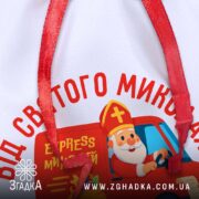 Мішечок від Миколая — крупний план тканини та друку, деталь логотипу “Express Миколай” і червоної стрічки.