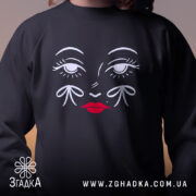 Світшот жіноче обличчя, чорного кольору, з ракурсу спереду, на однотонному фоні, принт з обличчям з білими деталями та червоними губами, кругла горловина, манжети з трикотажної резинки, фактура м'яка і комфортна.