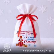 Торбинка Святого Миколая на білому фоні зі сніжинками та червоною стрічкою.