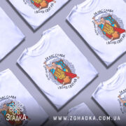 Футболка український козак, білого кольору, зображена з фронтального ракурсу на манекені, фон світло-сірий, принт з козаком, що тримає меч і щит з тризубом, оточений деревами та квітами, текст на футболці: 'За нас слава, за нас правда, і воля святая'.