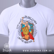 Футболка український козак, білого кольору, зображена зверху, складена на поверхні, фон світло-сірий, принт з козаком, що тримає меч і щит з тризубом, оточений деревами та квітами, текст на футболці: 'За нас слава, за нас правда, і воля святая', на футболці є етикетка з зеленим шнурком.