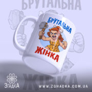 Чашка брутальна жінка, біла, зображення зліва, фон світло-сірий, принт з малюнком жінки в кам'яному віці з молотом, напис 'Брутальна жінка' синім кольором, ручка стандартна, край рівний, матова поверхня.