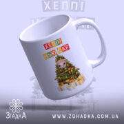 Чашка новорічна казка з подарунками, біла, з легким нахилом, на фоні світло-сірого кольору, принт з новорічною ялинкою та написом 'ХЕППІ НЬЮ ЄР', ручка округла, край гладкий, глянцева поверхня.