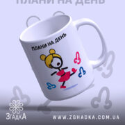 Чашка плани на день, біла з кольоровим принтом, зображення дівчини в червоній спідниці, ручка з правого боку, край рівний, матова поверхня, фон світло-сірий.