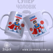 Чашка супер чоловік, дві білих чашки з малюнком супергероя, що стоять поруч, на фоні блакитного неба з хмарами та кольоровими цукерками, ручки круглі, краї рівні, глянцева поверхня.