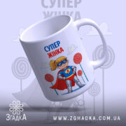 Чашка супер жінка, біла з яскравим принтом, показує супергероїню з жовтими волоссям у масці та червоному плащі, з легким нахилом, на фоні кольорових цукерок, ручка класична, край рівний, глянцева поверхня.
