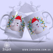 Чашка Веселий новорічний ведмедик, дві чашки в паралельному розташуванні, біла з яскравим принтом ведмедика у червоній шапці, ракурс з боку, фон з м'яким світлом, принт обрамлений різнокольоровими вогниками, ручки стандартні, краї рівні, глянцева поверхня.