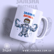 Чашка залізна дитина, біла з кольоровим принтом, показує персонажа з коротким волоссям у сірому костюмі, що тримає ланцюги. Ручка чашки гладка, край рівний, поверхня має глянець, фон світло-сірий з розмитим зображенням.