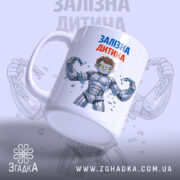 Чашка залізна дитина, біла з кольоровим принтом, показує персонажа з коротким волоссям у сірому костюмі, що тримає ланцюги. Ручка чашки гладка, край рівний, поверхня має глянець, фон світло-сірий з розмитим зображенням.