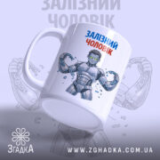 Чашка залізний чоловік, біла з кольоровим принтом, зображення залізного чоловіка з ланцюгами, ручка з правого боку, глянець на поверхні, фон світло-сірий з повторюючим малюнком.