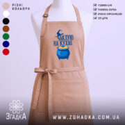 Фартух чаклую на кухні, бежевого кольору, зображений з фронтального ракурсу на манекені, фон нейтральний, принт з написом та зображенням казана з варивом.