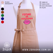 Фартух готую за поцілунки, бежевого кольору, зображений з фронтального ракурсу на манекені, фон світлий, принт з текстом червоного кольору та малюнком губ рожевого кольору.