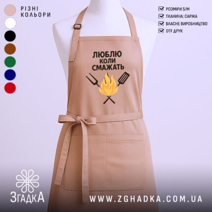 Фартух люблю коли смажать, бежевого кольору, зображений з фронтального ракурсу на манекені, фон світлий, принт з текстом та малюнком вогню і кухонних інструментів.