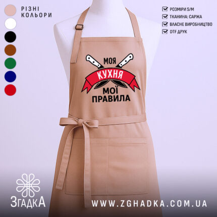 Фартух моя кухня мої правила. Фартух бежевого кольору, зображений з фронтального ракурсу на манекені. Фон світлий, без зайвих деталей. Принт містить напис 'Моя кухня мої правила' на червоному банері з зображенням ножів.
