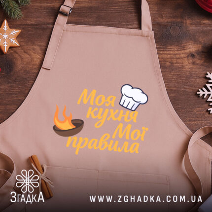 Фартух моя кухня, бежевий колір, зображення з верхнього ракурсу, фон дерев'яний, принт з написом 'Моя кухня Мої правила' та зображенням шеф-капелюха і вогню.