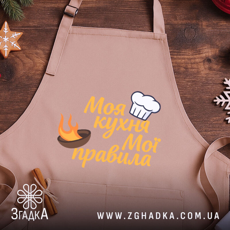 Фартух моя кухня, бежевий колір, зображення з верхнього ракурсу, фон дерев'яний, принт з написом 'Моя кухня Мої правила' та зображенням шеф-капелюха і вогню.