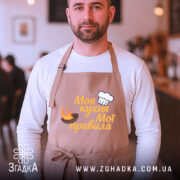 Фартух моя кухня, бежевий колір, зображення з фронтального ракурсу, фон кафе, принт з написом 'Моя кухня Мої правила' та зображенням шеф-капелюха і вогню.