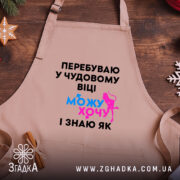 Фартух можу і хочу, бежевого кольору, зображений на дерев'яному фоні, деталі принта чорного кольору з яскравими елементами синього та рожевого.