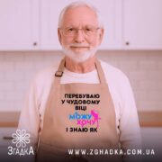 Фартух можу і хочу, бежевого кольору, зображений на дерев'яному фоні, деталі принта чорного кольору з яскравими елементами синього та рожевого.