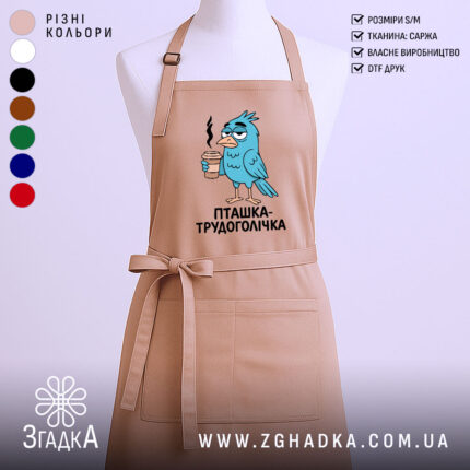Фартух пташка трудоголічка, бежевого кольору, зображений на манекені, фон світлий, принт з пташкою, що тримає каву, з виразом трудоголіка.