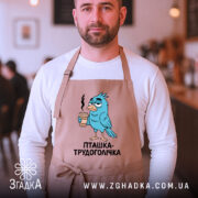Фартух пташка трудоголічка, бежевого кольору, на чоловікові, фон кафе, принт з пташкою, що тримає каву, з виразом трудоголіка.
