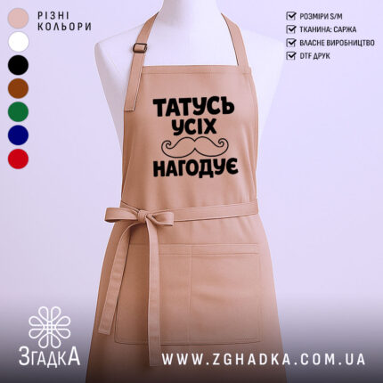 Фартух татусь усіх нагодує, бежевого кольору, зображений з фронтального ракурсу на манекені, фон світлий, принт чорного кольору з написом та малюнком вусів.