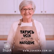Фартух татусь усіх нагодує, бежевого кольору, зображений з фронтального ракурсу на манекені, фон світлий, принт чорного кольору з написом та малюнком вусів.
