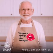 Фартух цілуюся краще ніж готую, бежевого кольору, зображений з верхнього ракурсу на дерев'яному фоні, деталі принта включають червоні губи та чорний текст, поряд з декором у вигляді зірочки та кориці.