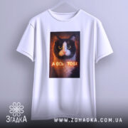 Футболка а ось тобі біла, підвішена на вішалці, ракурс спереду, принт кота з написом "А ОСЬ ТОБІ" на грудях.