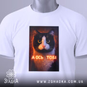 Футболка а ось тобі біла, складена, з принтом кота, ракурс зверху, на комірці видно етикетку, напис "А ОСЬ ТОБІ" на принті.
