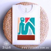 Футболка абстрактне арт зображення, біла, складена на плетеній кошику, фон білий, принт містить стилізовану фігуру людини в блакитному, червоному та бежевому кольорах.