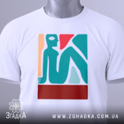 Футболка абстрактне арт зображення, біла, складена на поверхні, фон світло-сірий, принт зображує стилізовану фігуру людини в блакитному, червоному та бежевому кольорах, з етикеткою на шнурку.