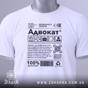 Футболка адвокат білого кольору, зображена зверху на столі, фон світлий, принт з текстом та символами, на комірці є етикетка з зеленим шнурком.