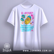 Футболка акушер, біла, зображена на манекені, фон світло-сірий, принт з мультяшним малюнком немовляти в ковдрі, з червоним серцем та кольоровими елементами, рукава короткі.