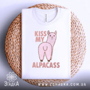 Футболка альпака гумор, біла, складена на плетеному кошику, фон білий, принт з альпакою та написом 'KISS MY ALPACASS' у рожевих тонах.