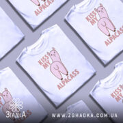 Футболка альпака гумор, біла, зображена на манекені з правого боку, фон світло-сірий, принт з веселим альпакою та написом 'KISS MY ALPACASS' у рожевих тонах.