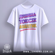 Футболка аналітик не токсік, біла, підвішена на вішалці, фон світло-сірий, принт з текстом "ДИШИНА ТОКСІК АНАЛІТИК" з перекресленим словом "ТОКСІК", кольори фіолетовий та жовтий.