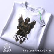 Футболка ангел боєць білого кольору, складена на столі, фон світло-сірий, принт з зображенням ангела-борця з крилами та автоматом, напис 'ANGEL' під малюнком, на футболці є етикетка з зеленим шнурком.